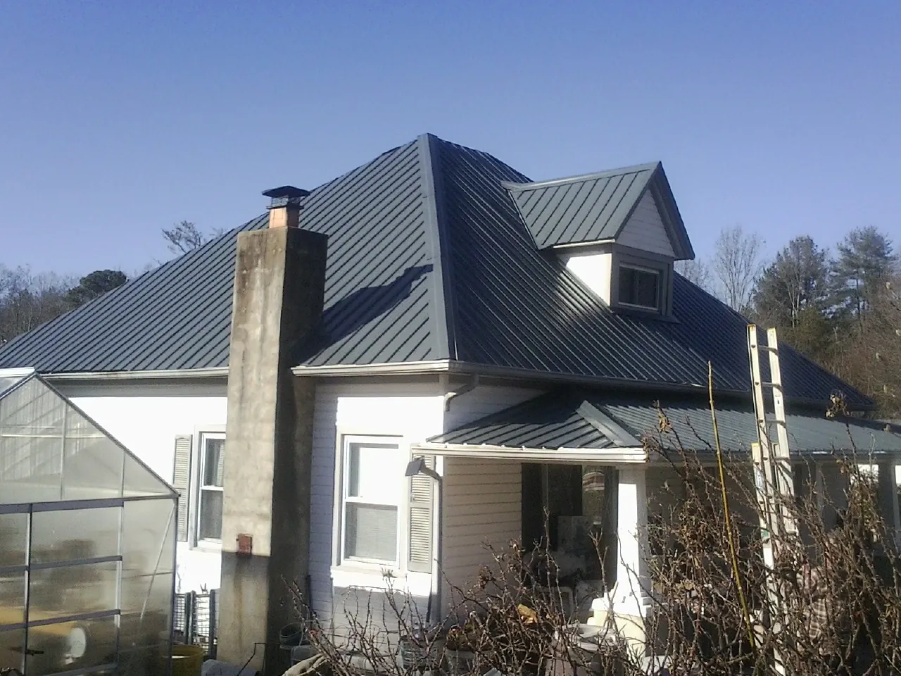 Dark blue standing seam metal roof on a white farmhouse with dormer — Slate & Tile Roof Repair by Roofing Brothers in La Harpe