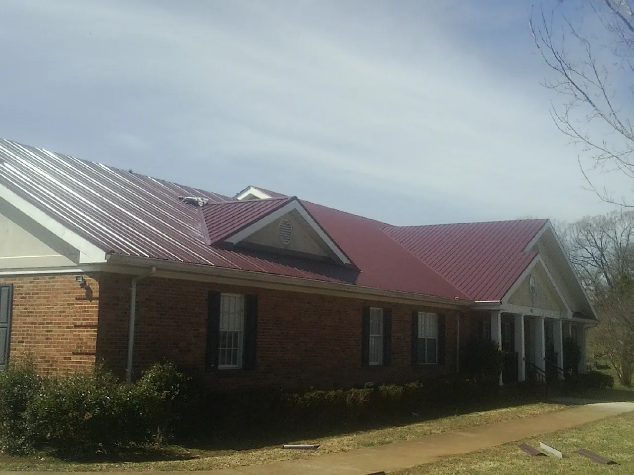 Red metal roof with gabled entries on a long brick building, from a Hail Damage Roof Repair job in La Harpe