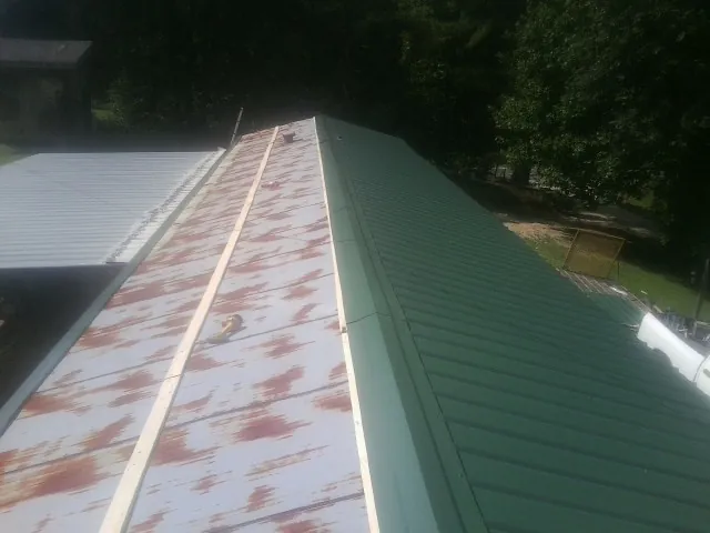 Old rusted panels beside newly installed green metal roofing — Wind Damage Roof Repair by Roofing Brothers in La Harpe