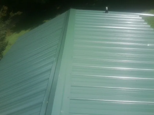 New green metal panels meeting at the ridge of a roof — Flat Roof Repair work by our crew in La Harpe