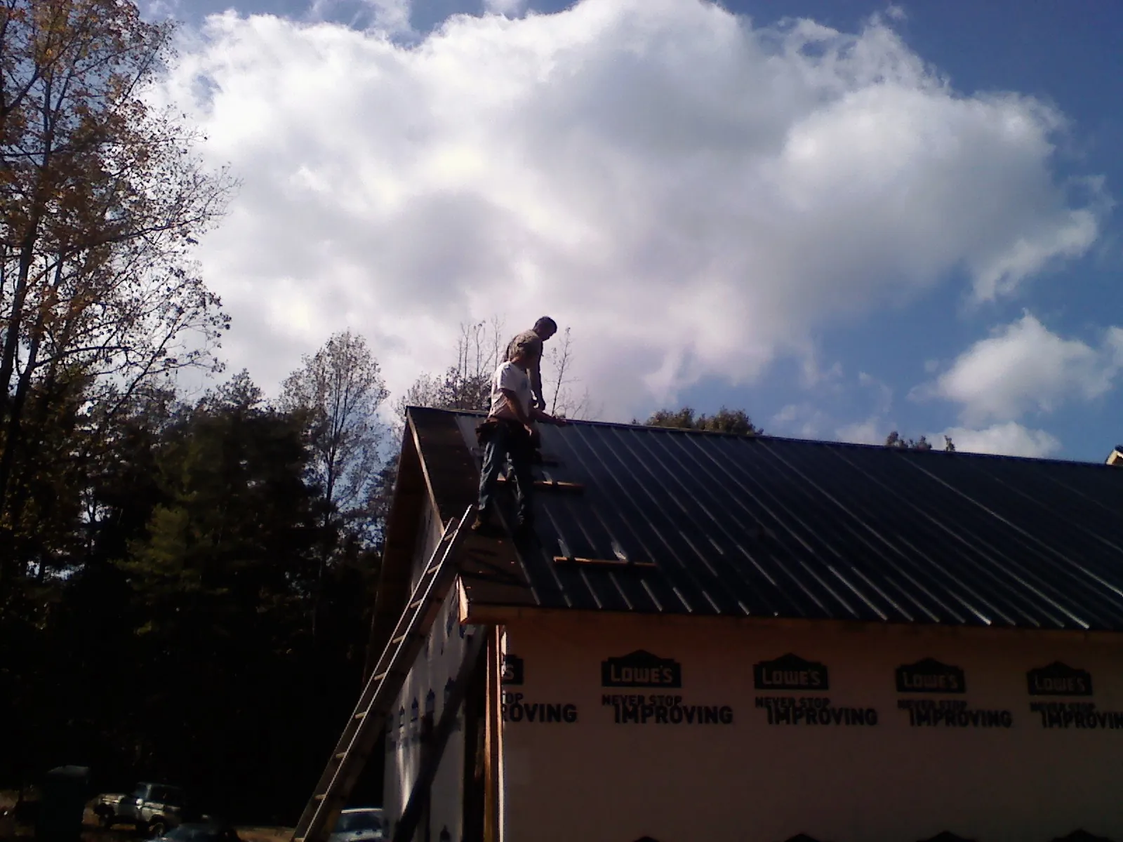 Roofer fastening dark metal panels high against a cloudy sky, from a Roof Inspection job in La Harpe