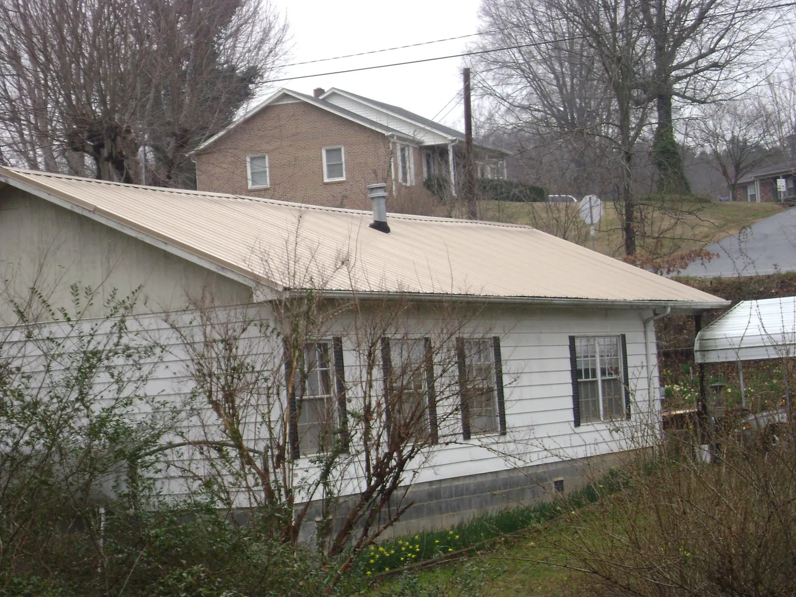 Tan metal roof on a white sided house set into a hillside — Commercial Roofing by Roofing Brothers in La Harpe