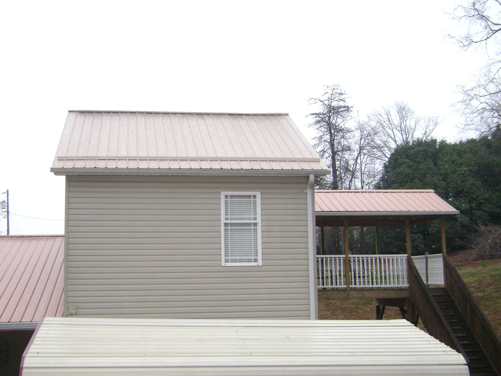 Tan metal roofs on a two story addition and attached porch, from a Roof Replacement job in La Harpe